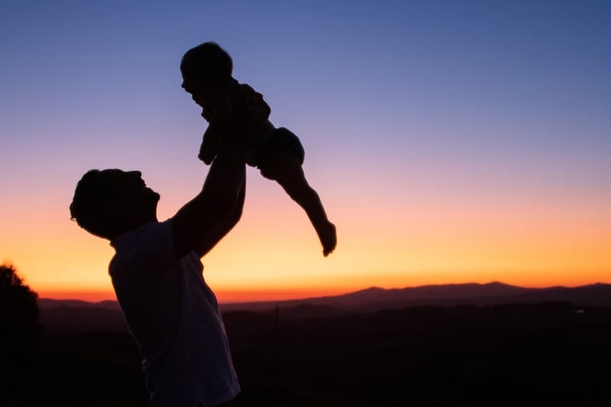 Homem simbolizando um pai e criança um filho com um pôr do sol atrás