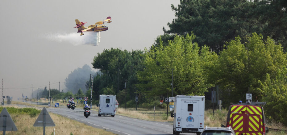 A Canadair plane drops water along the departmental road 112 while a fire is currently heading towards the town of Cazaux which was evacuated in the early afternoon, in La Teste-de-Buch, southwestern France, on July 14, 2022. - Firemen are facing on July 14, 2022 a "negative situation" as they fight two forest fires that have destroyed 4200 hectares since July 12, 2022, including more than 2000 hectares in La Teste-de-Buch. (Photo by THIBAUD MORITZ / AFP)