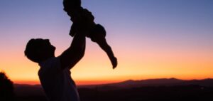 Homem simbolizando um pai e criança um filho com um pôr do sol atrás